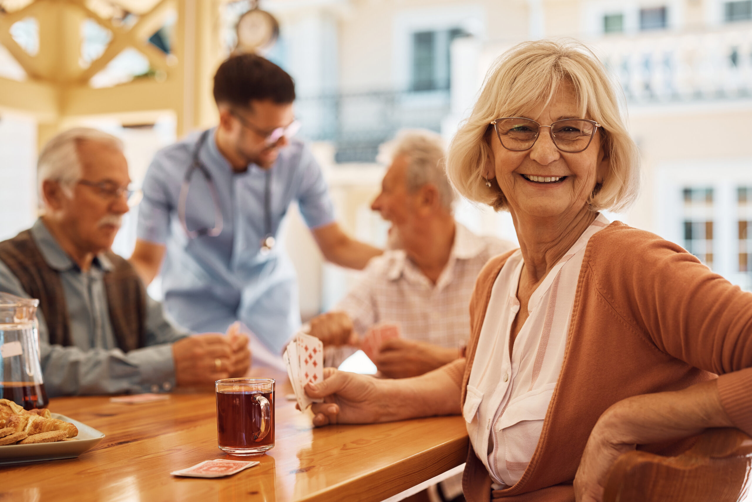 A group who has decided between independent living vs. assisted living sits around the breakfast table playing cards.